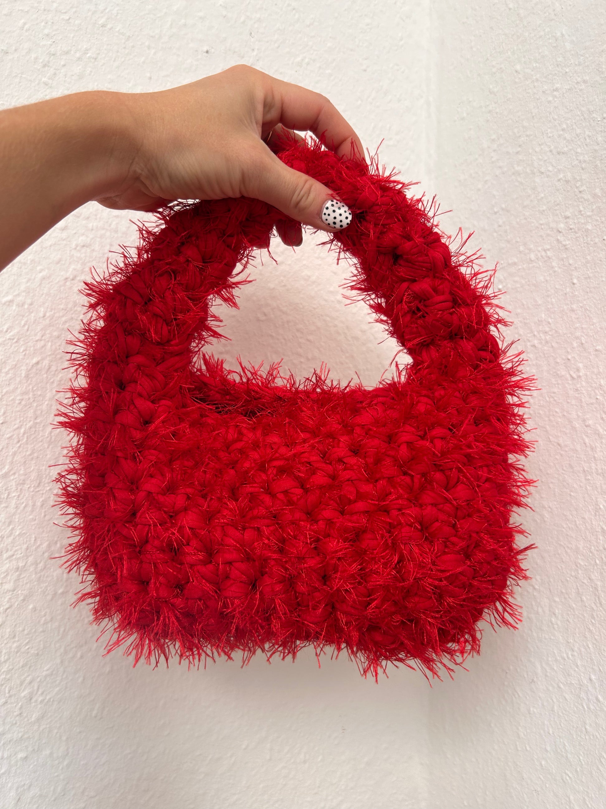 Red textured handbag held by a hand against a white background