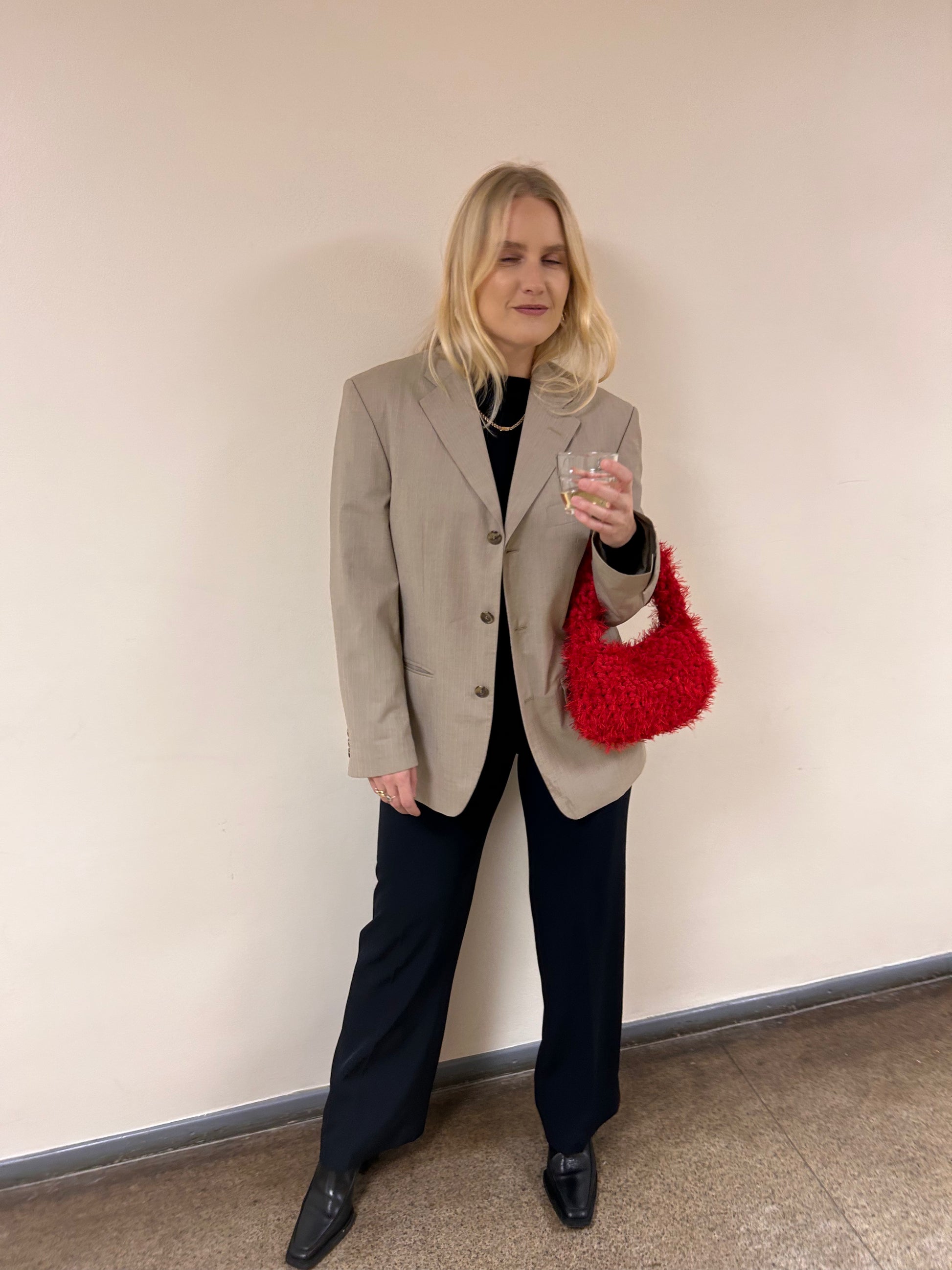 Woman holding a red handbag against a plain wall