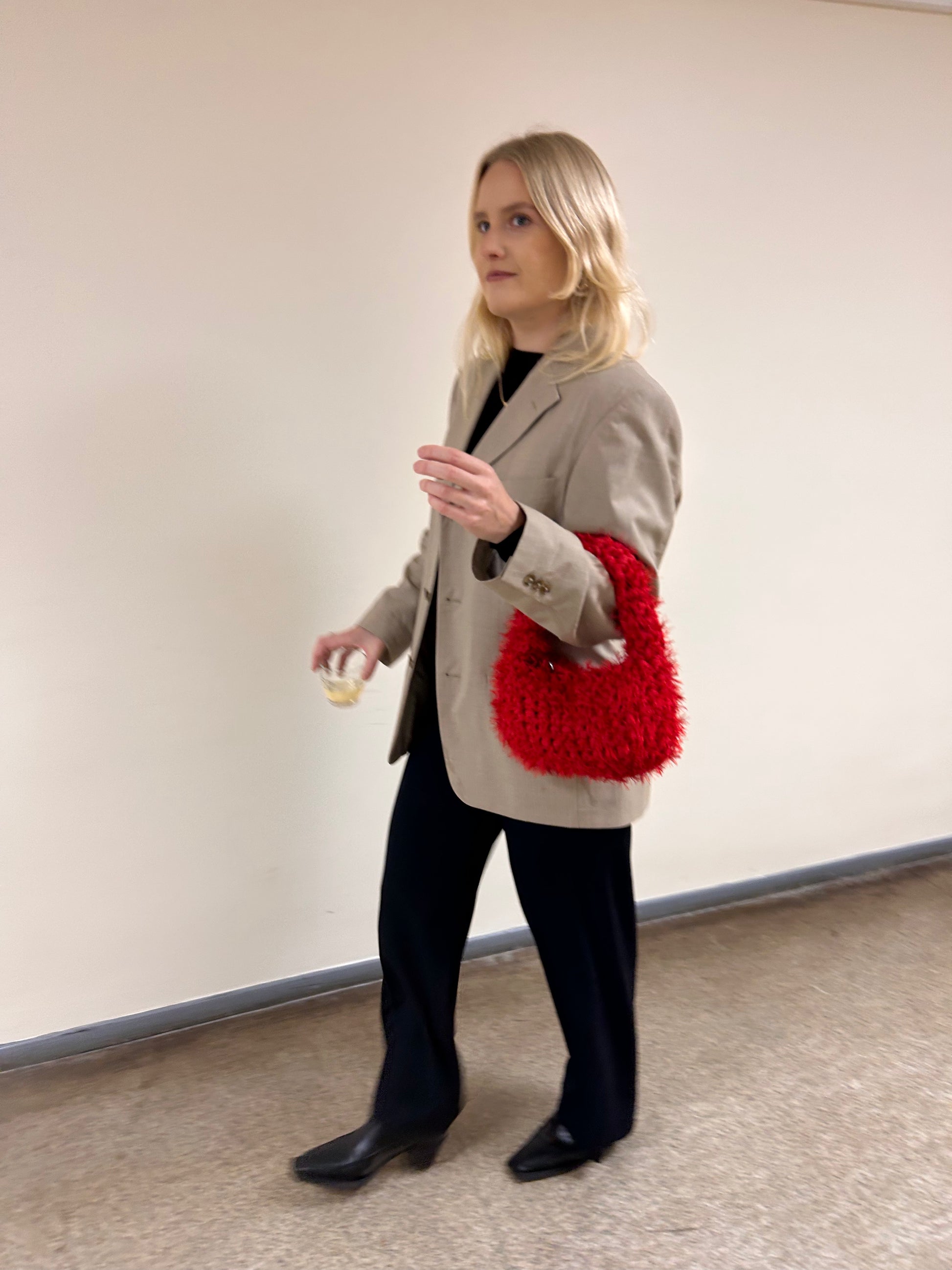 Woman holding a red knitted bag against a plain background