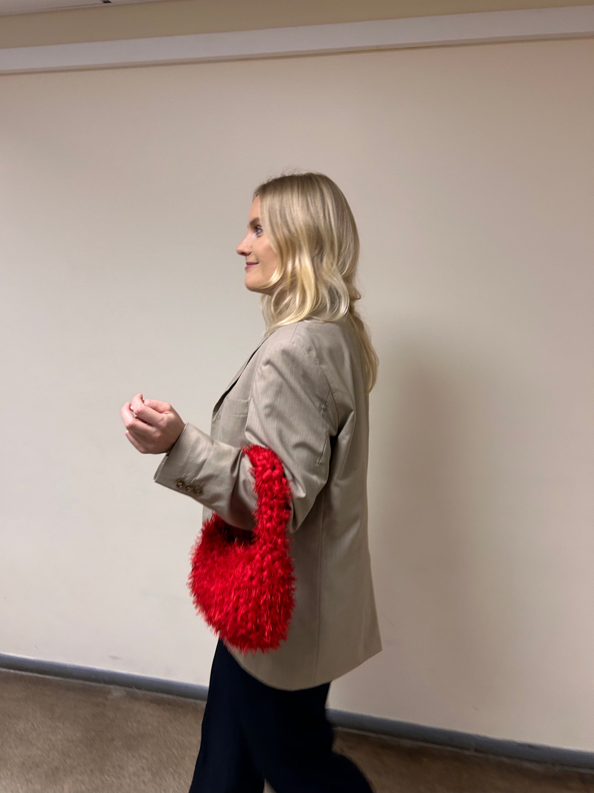 Woman holding a red textured bag against a plain wall