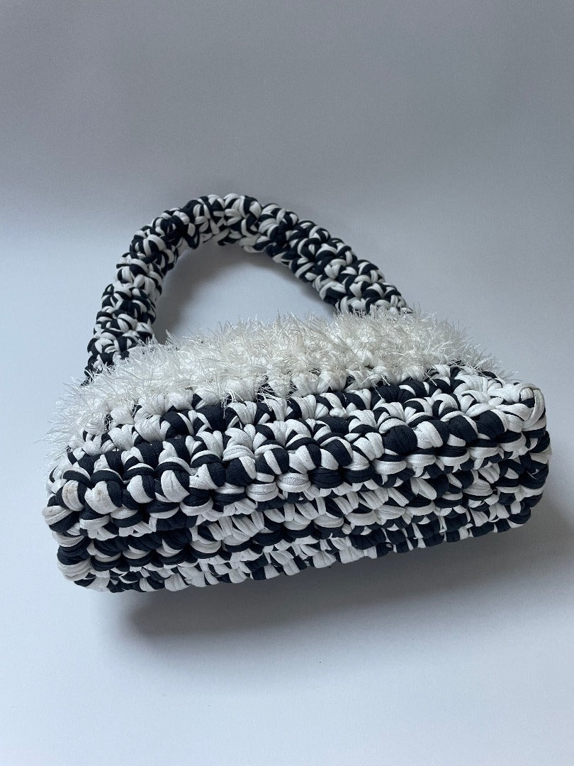 Black and white crochet bag with white fluffy detailing in the middle, shot sideways