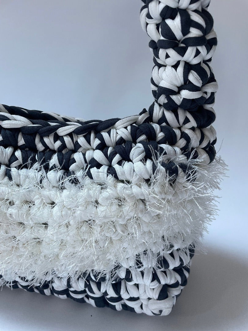 Closeup of black and white crochet bag with white fluffy detailing in the middle