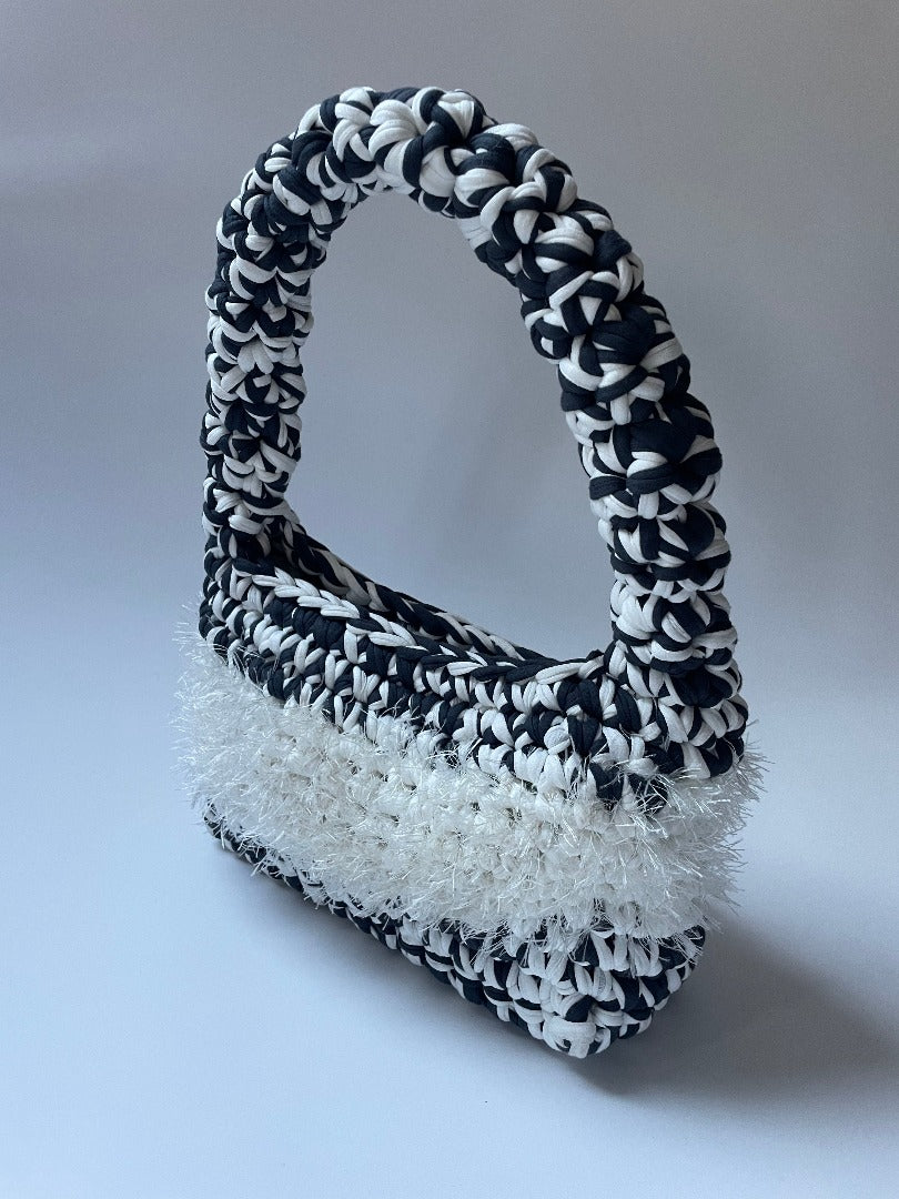 Black and white crochet bag with white fluffy detailing in the middle, shot from the side