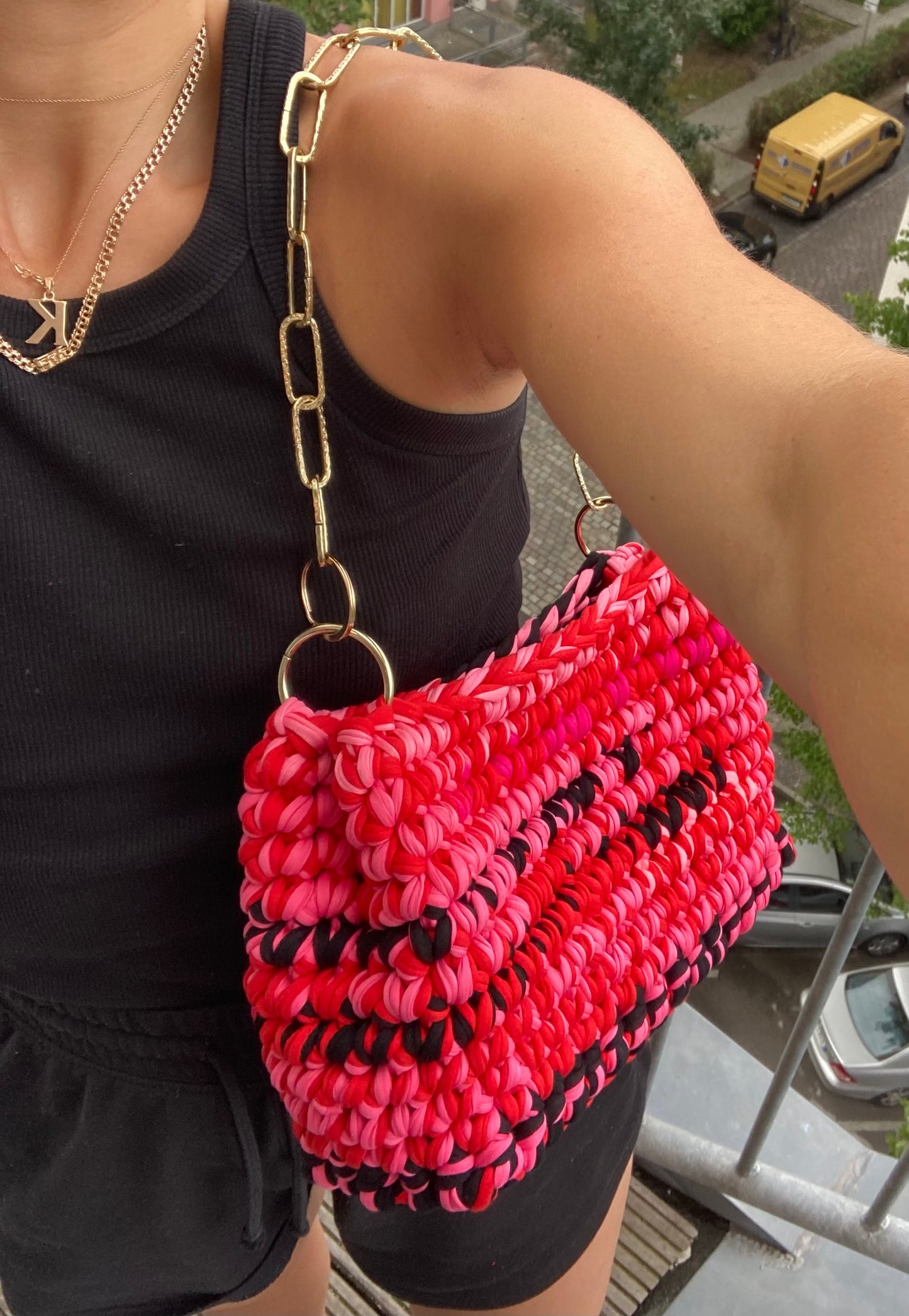 A person standing wearing a pink and red crochet bag with black detailing, black shorts and black tank top.